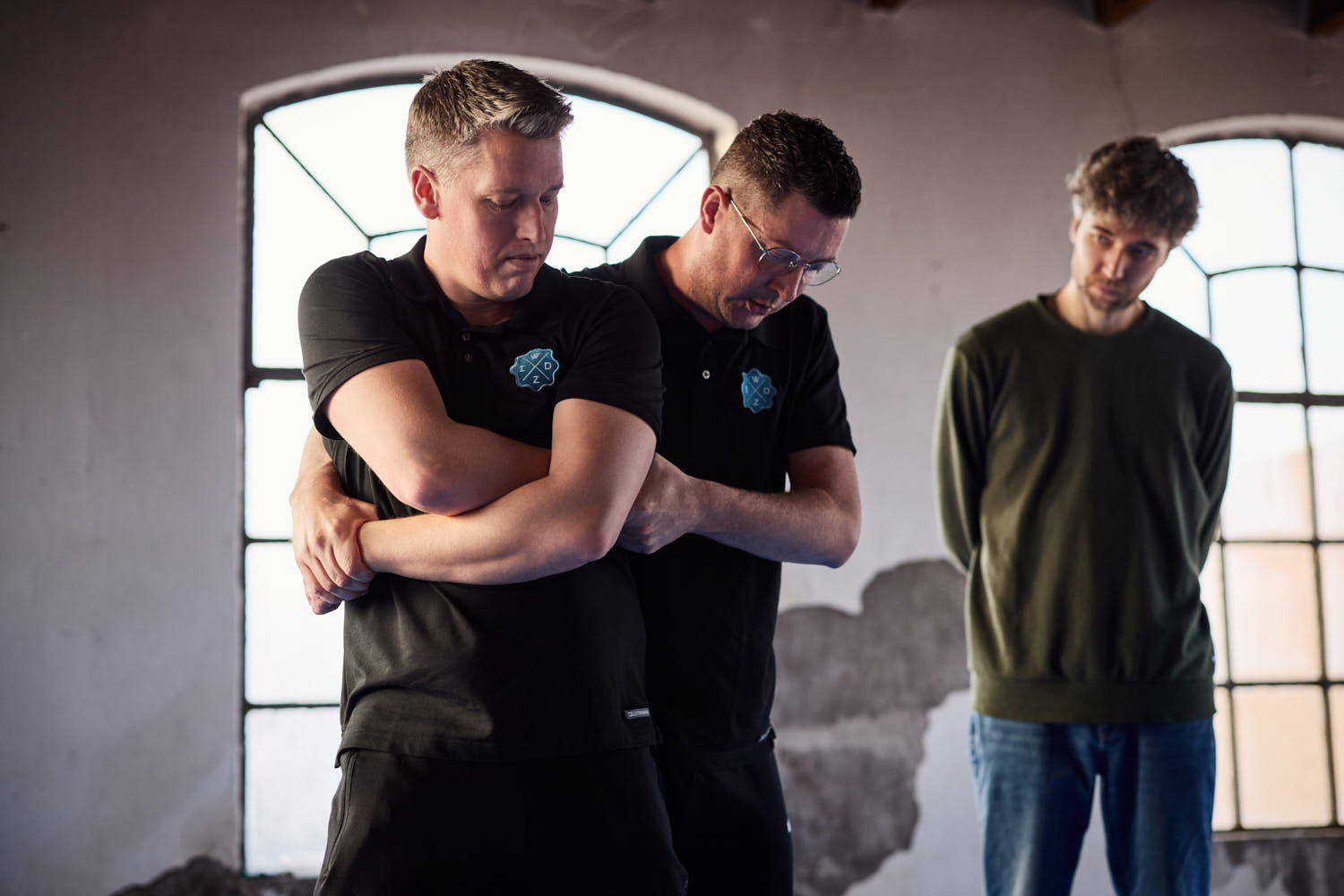Twee trainers demonstreren een veilige omklemming tijdens een weerbaarheidstraining